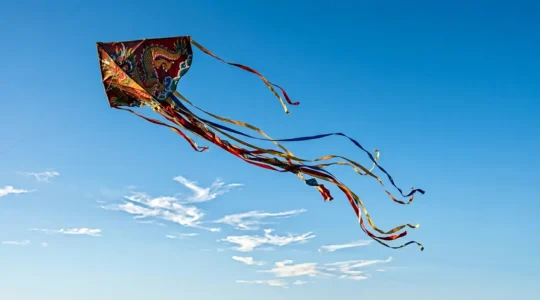 Cerf-volant traditionnel asiatique traçant des courbes élégantes dans le ciel bleu, évoquant l'art de la calligraphie