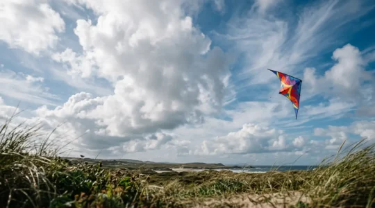 Cerf-volant coloré planant dans un ciel parsemé de cumulus, symbolisant la connexion entre l'homme et les éléments naturels