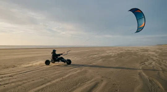 Pilote de kite buggy sur une plage dégagée, aile de traction déployée dans un vent modéré