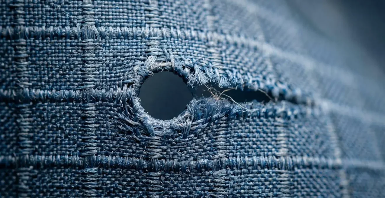 Gros plan macro sur une déchirure de tissu ripstop montrant la concentration des contraintes