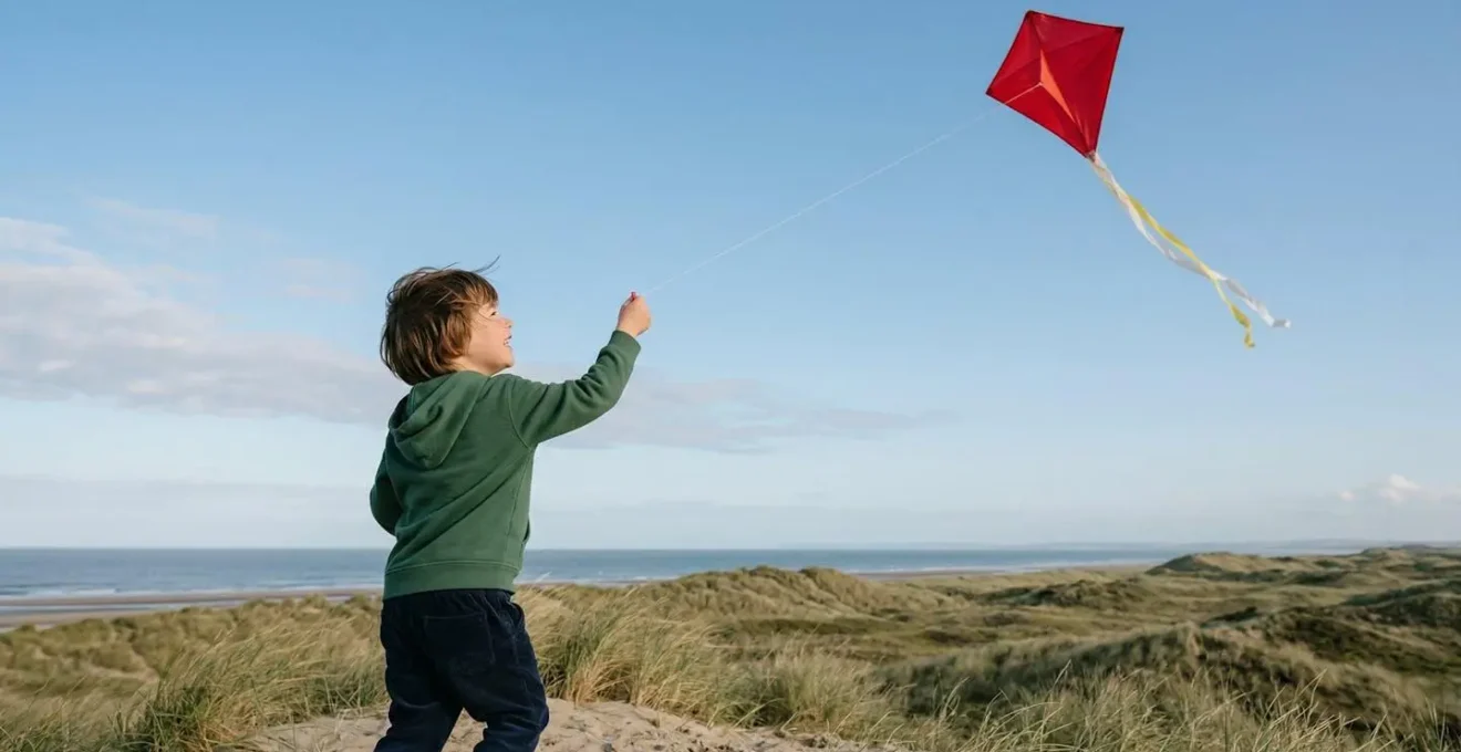 Enfant de 5 ans faisant voler un cerf-volant diamant rouge dans un ciel bleu dégagé