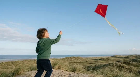 Enfant de 5 ans faisant voler un cerf-volant diamant rouge dans un ciel bleu dégagé