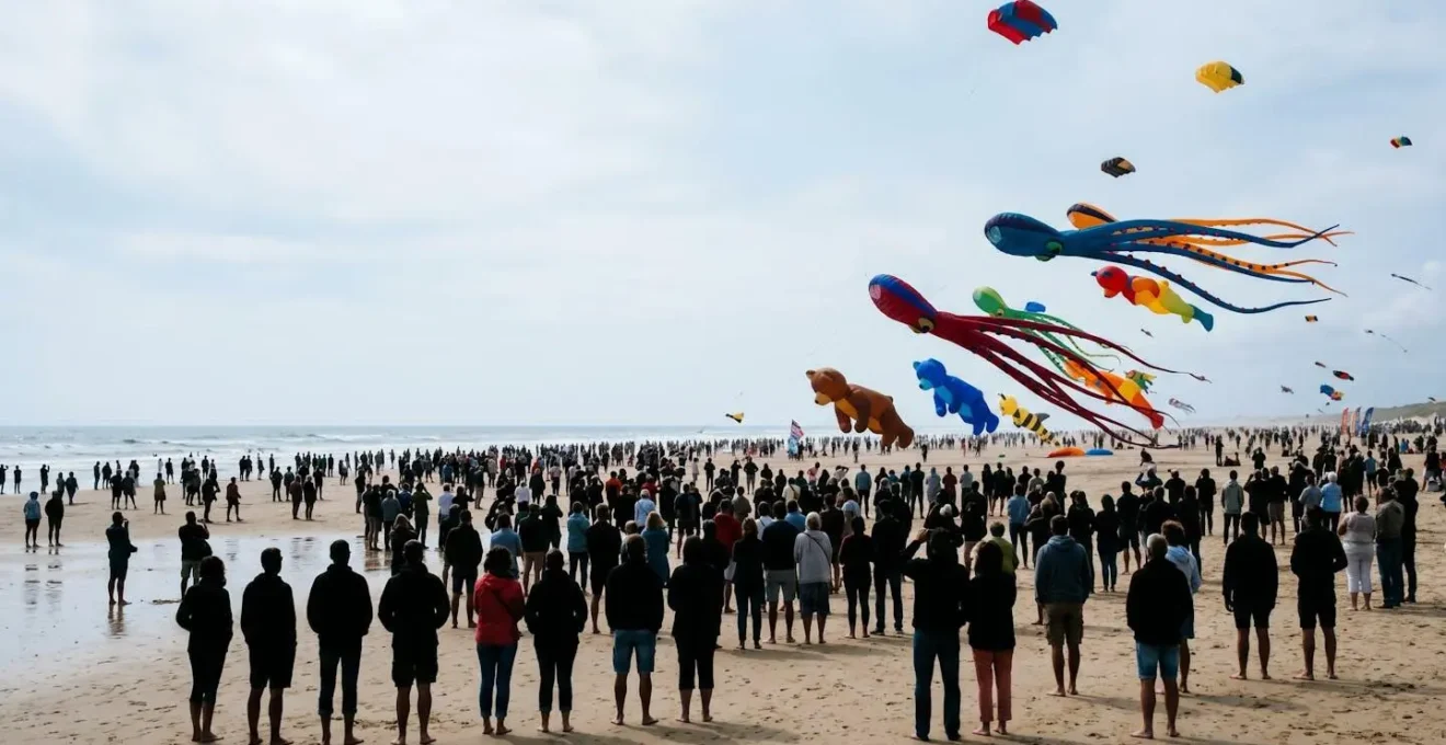 Vue grand angle d'une foule admirant des cerfs-volants géants sur une plage, atmosphère festive et colorée