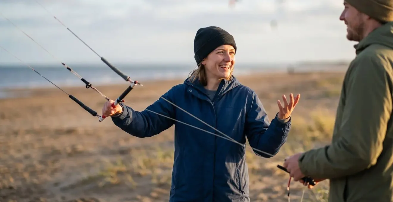 Pilotes de cerfs-volants communiquant par gestes sur une plage venteuse pour coordonner leurs vols