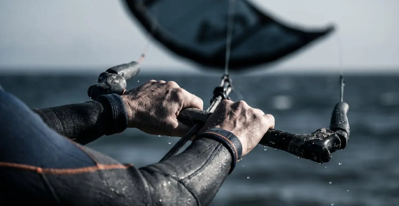 Gros plan sur des mains tenant une barre de contrôle de kitesurf avec l'aile visible en arrière-plan dans la zone de puissance critique